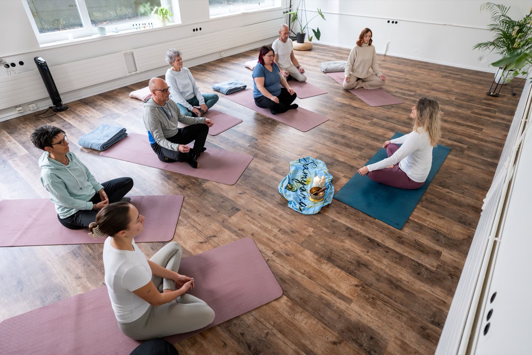 Workshop-Gruppe sitzt im Kreis auf Matten im hellen Raum — gemeinsames bewusstes Atmen.