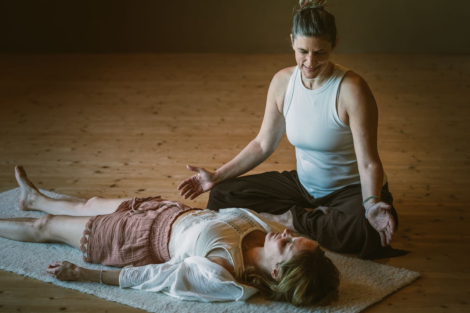 Caroline begleitet eine Breathwork-Session — sitzend neben einer Person auf einem Schaffell, warmer Holzboden.