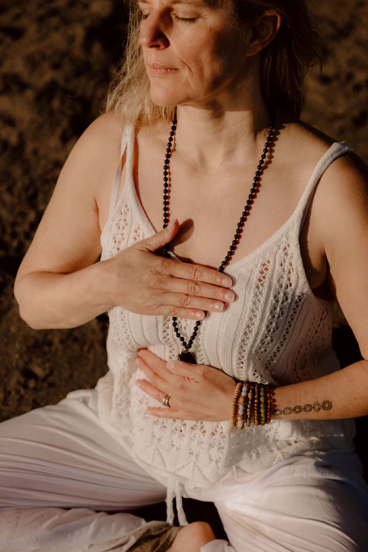Caroline in der Meditation, eine Hand auf dem Herzen, eine auf dem Bauch — bewusste Atmung im Abendlicht.